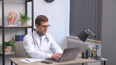 Doctor man sitting at the desk at his working place and working on laptop. Perfect medical service in clinic. Happy future of medicine and healthcare