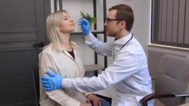 A young attractive otolaryngologist examining nose of a young patient during a medical examination in the ENT office