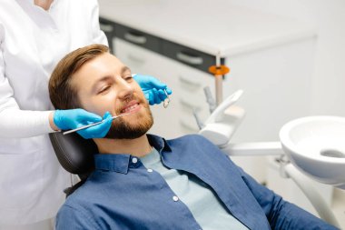 Modern klinikte dişçi koltuğunda oturup gülümseyen mutlu bir adamın portresi. Profesyonel dişçide diş tedavisinden hoşlanan hasta.