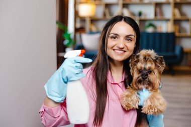 Evdeki temizlik malzemelerinin yanındaki masaya yaslanan genç bir kadın ve küçük köpeği onun yanında duruyor..