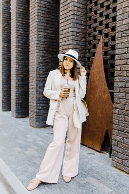 Beautiful woman going to meeting with cold coffee walking on the street. Portrait of successful business woman holding cup of cold drink in hand on her way to work on city street
