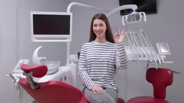 歯医者の診察後は若い笑顔の幸せそうな女の子が歯科医院の椅子に座る 歯の治療 — ストック動画