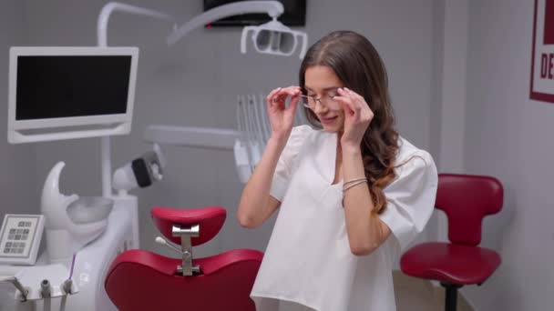 若い医師が歯医者のオフィスで眼鏡をかけている 歯科クリニックで眼鏡をかけている女性医師の肖像画 歯科オフィスで医療ユニフォームを着用している医療従事者 — ストック動画