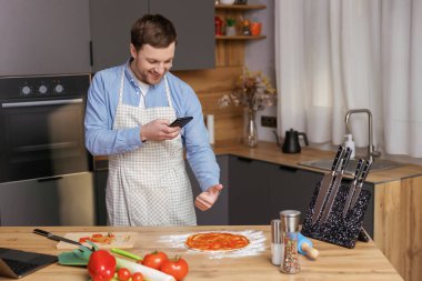 Yakışıklı adam mutfakta yemek pişiriyor ve cep telefonunda yemek hazırlıyor.