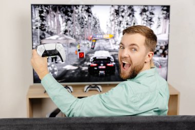 Genç adam evde vakit geçiriyor, kanepede oturuyor ve konsolda video oyunları oynuyor. Oyun oynamak ve kazanmak için joystick kullanan başarılı bir erkek..