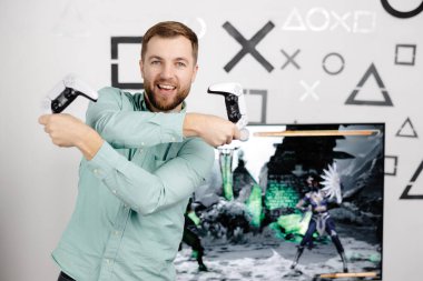 Genç sakallı adam odanın duvarında duruyor ve oynuyor, elinde kablosuz kumanda, çığlık atıyor ve yoğun bir video oyunu maçı kazanıyor.