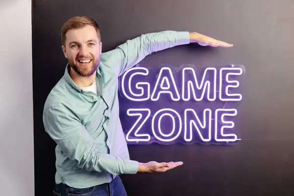 A young handsome man is standing near a wall with the inscription game zone