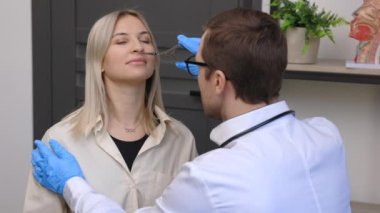 A young attractive otolaryngologist examining nose of a young patient during a medical examination in the ENT office