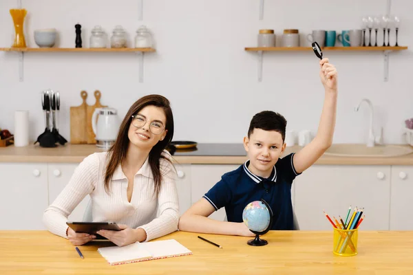 A young woman helps a boy with his lessons using a tablet and a globe. A homeschooling student does his homework with the help of a tutor.