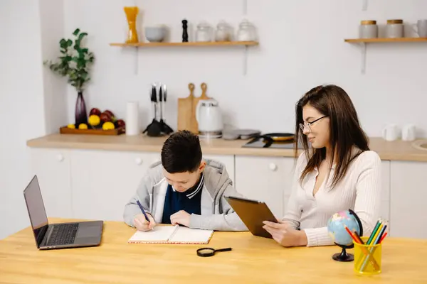 A young woman helps a boy with his lessons using a tablet and a globe. A homeschooling student does his homework with the help of a tutor.
