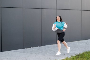 Zıplayan ve karanlık duvarlara karşı koşan zinde genç bir kadın. Spor giyiminde kadın modeli dışarıda egzersiz yapıyor.