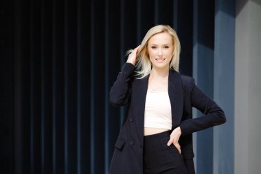 Siyah takım elbiseli güzel ve şık bir iş kadını şehrin gri duvarının yanında duruyor..