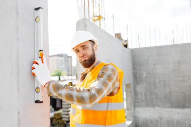 İnşaatçı-tamirci, ustabaşı, koruyucu bir miğferle beton bir binanın merdivenlerini kontrol eder..