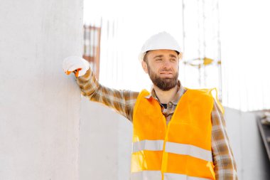 İnşaatçı, miğfer ve yelek giyen ustabaşı inşaat halindeki bir binada iş yerinde çalışıyor..