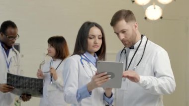Bir grup doktor gelecekteki operasyonlar hakkında konuşuyor, tablete bakıyor, x ışını fotoğrafındaki verileri inceliyor.