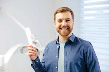 Handsome male patient looking at his beautiful smile standing at the dental office.