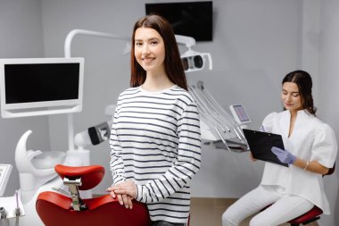 Doktor hastanın sağlığı hakkında notlar alırken genç ve güzel bir kız ofiste diş hekiminin yanında duruyor..