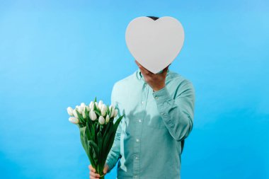 Elinde lale buketi ve hediye kutusu olan bir adam mavi arka planda izole edilmiş kameraya bakıyor. Kutlama konsepti.