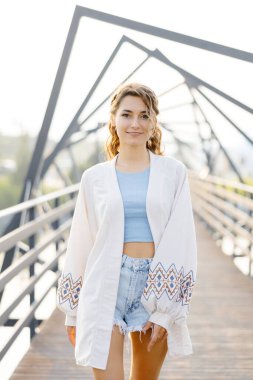 Beyaz hırka giyen bir kadın köprüde duruyor. Önüne bakarken sakin ve rahat görünüyor..