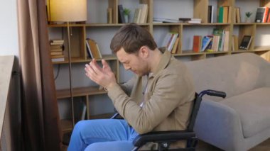 Tekerlekli sandalyedeki genç ve yakışıklı bir adam üzgün bir bakışla pencereden dışarı bakar.