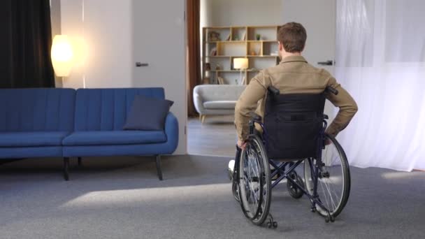 一个坐在轮椅上的英俊年轻人在公寓里走来走去 开始适应新的生活 受伤或在家中孤独寂寞后康复 — 图库视频影像