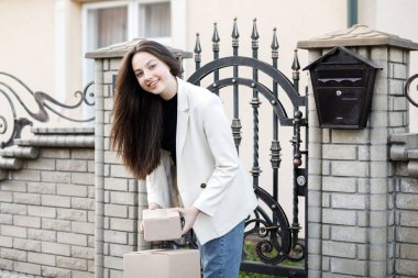 Elinde bir yığın karton kutuyla eve paket taşıyan genç bir kadın..