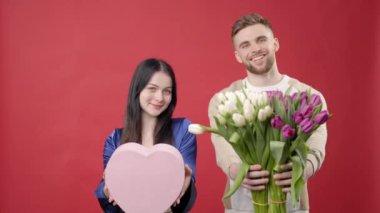 Gülümseyen sakallı adam güzel bir kadın için çiçek buketi ve hediye kutusu veriyor. Arka planda izole edilmiş mutlu romantik çiftin doğum günü portresi