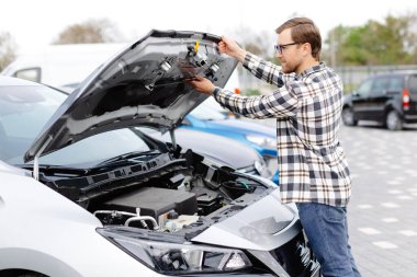 Genç adam arabanın kaputunun altını kontrol ediyor. Sorunun ne olduğunu anlamak için.