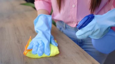 Koruyucu eldivenli kadın gülümsüyor ve evini temizlerken toz bezi kullanıyor.