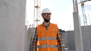 İnşaat tamircisi, koruyucu miğfer ve yelek giyen ustabaşı inşaat halindeki işyerinde duruyor.