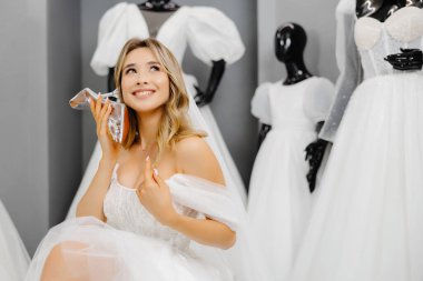 Müstakbel gelin bir kuaför salonunda gelinlik giyiyor, düğün için ayakkabı seçiyor ve telefon olarak ayakkabıyı kullanıyor..