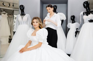 Müstakbel gelin, gelinlik almak için gelinlik salonuna geldi. Güzel bir kadın kuaförde gelinlik seçer ve bir asistan gelinin takmasına yardım eder..