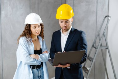 Çekici genç bayan müteahhit kasklı müşteriyle konuşuyor ve oturma odasında dizüstü bilgisayarla onarım sekansı gösteriyor. Ev sahibinin mühendis ya da mimarla görüşmesi