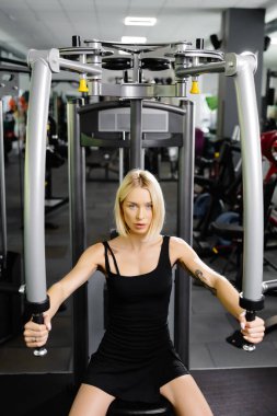 Güzel ve güçlü atletik kadın spor salonunda kas gruplarını pohpohlamak için simülatör kullanıyor..