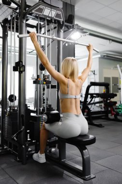 Gri takım elbiseli kadın spor simülatörünü spor salonunda çekmiş. Sırt kasları çok gergin.