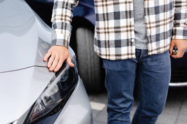 Galeride yeni arabasını kucaklayan sakallı genç adam neşeyle gülümsüyor..