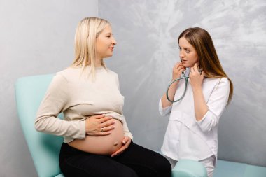 Steteskop kullanan kadın doktor klinikte hamile kadını muayene ediyor. Tıbbi muayene hamile kadın..