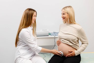 Doktor hamile bir kadını fetal monitörle fetüsün kalp atışlarını kontrol etmeye hazırlıyor.