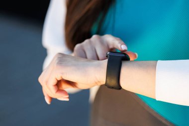 Kadın ellerindeki nabzı ölçmek için akıllı bir saat kullanıyor. Sokakta spor yapan bir kadın. Fitness ve sağlıklı bir yaşam tarzı.