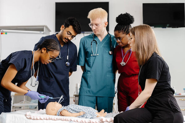 Четыре студента-медика в униформе собрались вокруг тренировочного манекена, чтобы практиковать техники реанимации.