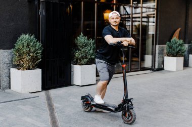 Tekmeli scooter kullanan hoş, gülen bir adam. Mutlu adam scooter sürüyor.