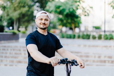 Young handsome man in white baseball cap riding on scooter to work along the street in the city. Active lifestyle, backpacker traveler. Ecology and clean ecological mode of transport