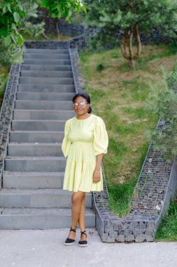 Koyu tenli bayan dışarıda gülüyor. Sarı elbiseli esmer kadın gülümsüyor ve dışarı çıkıyor..