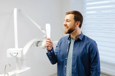 Handsome male patient looking at his beautiful smile standing at the dental office.