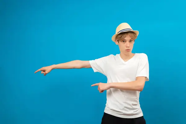 Stock image Young teen man points palms aside isolated on blue. Friendly well-looking boy paying your attention at copy space, best deal, sale, presenting novelty