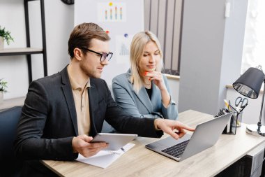 Modern ofis içinde buluşmaya başla, laptop ve tablet üzerinde çalış. Genç bir kadın ve bir adam masada oturuyor ve bir iş projesi üzerinde çalışıyorlar..