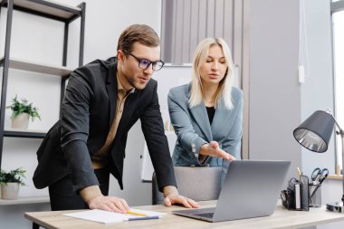 Concentrated male businessman looking at computer monitor, working with a young female worker on a project, people holding a video meeting with a client or interviewing a job candidate