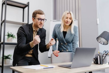 Concentrated male businessman looking at computer monitor, working with a young female worker on a project, people holding a video meeting with a client or interviewing a job candidate