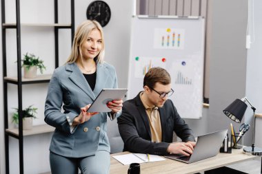 Resmi olarak çalışan neşeli genç şirket avukatları modern ofiste dizüstü bilgisayarla masada oturarak yeni sözleşmenin kurgu metnini giyerler. Kadın bir meslektaşının yanında oturuyor ve elinde bir tablet tutuyor..