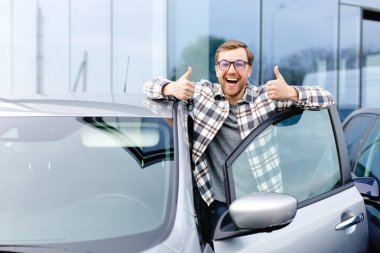 Otomobilin yanında duran neşeli adam, galeri merkezinde araba alırken işaret veriyor.